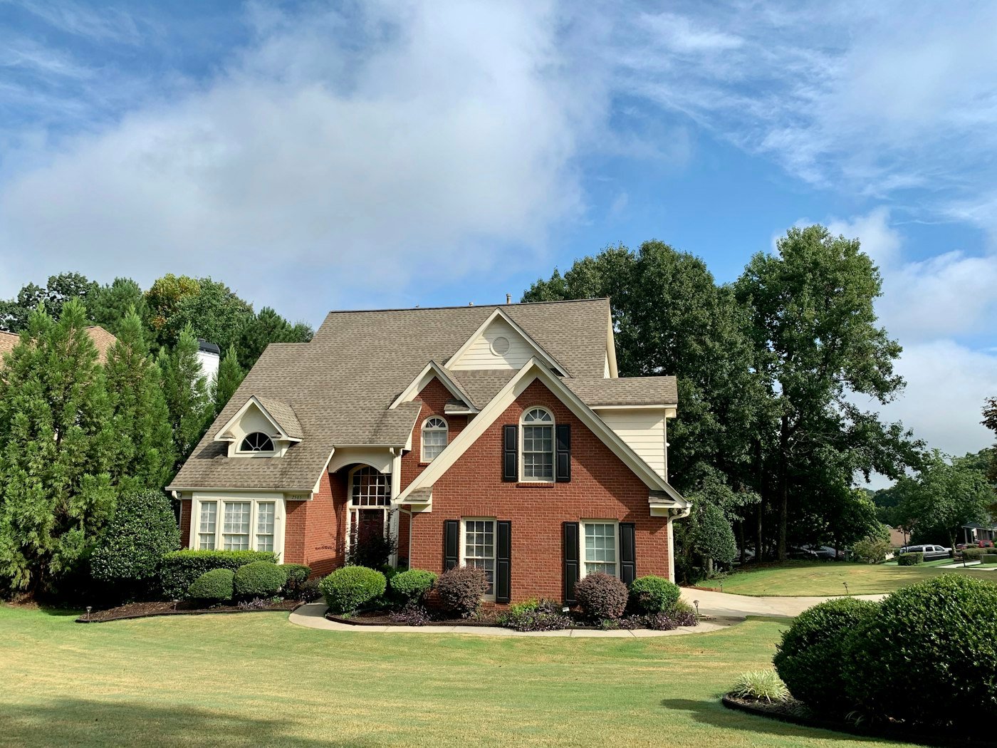 A red brick house with a grey roof, black shutters, and a curved lawn